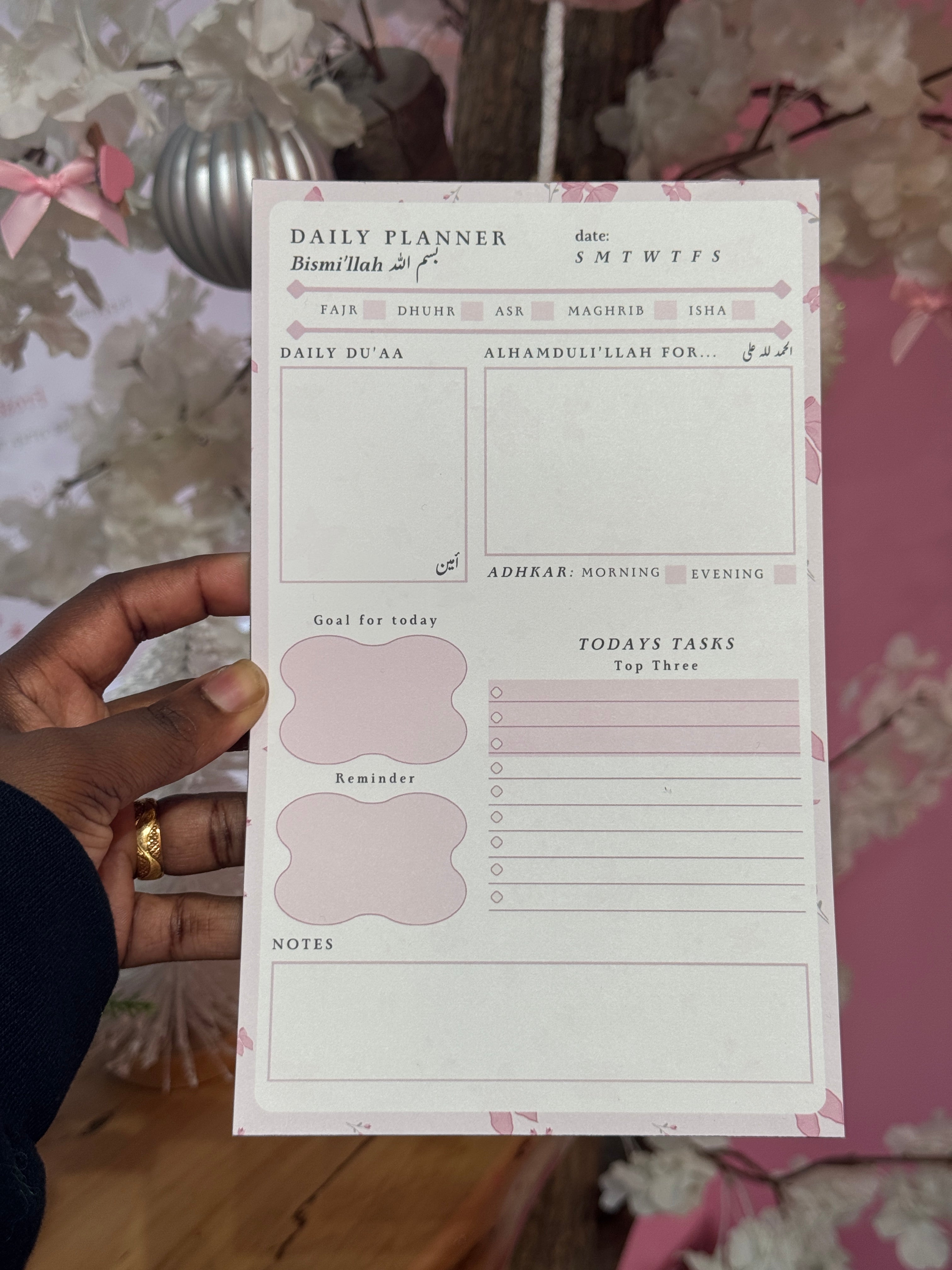 Hand holding a planner sheet with floral and minimalistic design. coquette daily planner. pink daily planner. islamic stationery. 